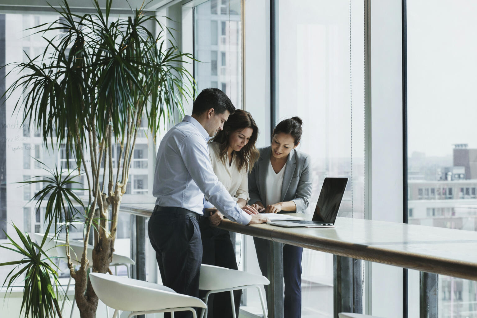 Work Clarity Series - Practical Tools for Navigating Difficult Work Environments Three professionals standing in a bright office reviewing documents together in a calm, focused discussion